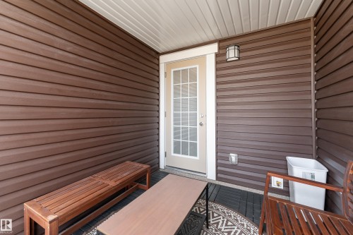 Outdoor patio featuring dark wood-finish siding, a white privacy door, an overhead light fixture, and a slatted ceiling - 20247 16 Avenue Nw, Edmonton, AB 