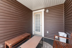 Outdoor patio featuring dark wood-finish siding, a white privacy door, an overhead light fixture, and a slatted ceiling - 