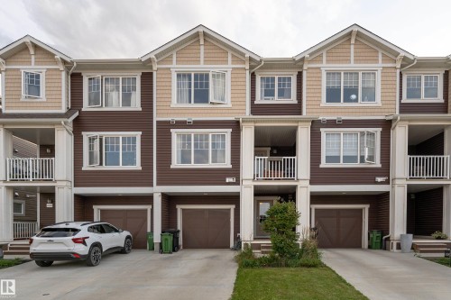 Multi-level townhome featuring a brown and tan exterior, multiple white-framed windows, integrated single-car garages, and covered balconies with white railings - 20247 16 Avenue Nw, Edmonton, AB 