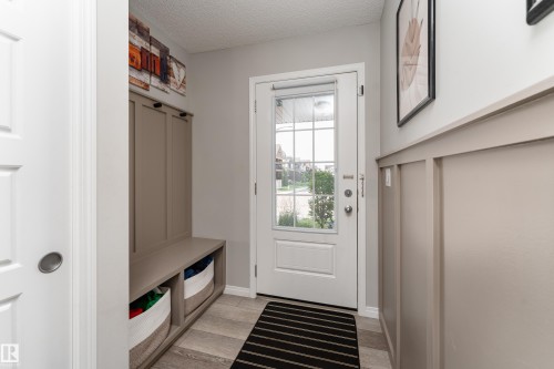 Entryway featuring a white door with divided lites, built-in mudroom storage, wood-finish flooring, and panel molding - 20247 16 Avenue Nw, Edmonton, AB 