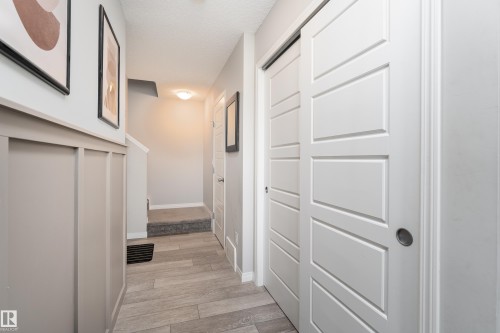 Wood-finish flooring throughout, featuring a wainscoting accent wall and modern white sliding panel doors - 20247 16 Avenue Nw, Edmonton, AB 
