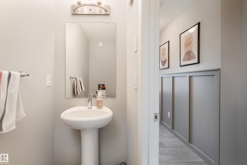 Pedestal sink with chrome faucet, rectangular mirror, and a wall-mounted light fixture - 20247 16 Avenue Nw, Edmonton, AB 
