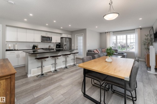 Spacious open-concept living area with wood-finish flooring, recessed lighting, and a large multi-pane window - 20247 16 Avenue Nw, Edmonton, AB 