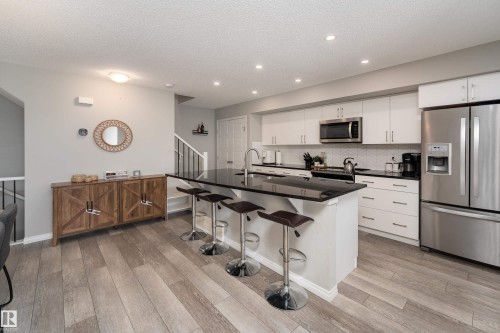 Well-appointed kitchen featuring wood-finish flooring, white cabinetry, a black island countertop, stainless steel appliances, and recessed lighting - 20247 16 Avenue Nw, Edmonton, AB 
