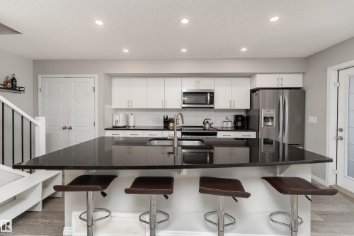 Modern kitchen featuring white cabinetry, stainless steel appliances, a dark countertop island, a herringbone tile backsplash, and recessed lighting - 20247 16 Avenue Nw, Edmonton, AB 