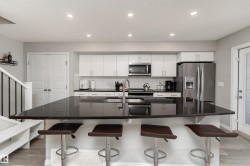 Modern kitchen featuring white cabinetry, stainless steel appliances, a dark countertop island, a herringbone tile backsplash, and recessed lighting - 