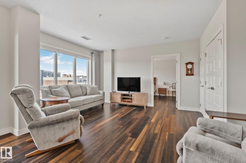 Expansive living area featuring wood-finish flooring, a full wall of windows, and white trim - #404 2755 109 St Nw, Edmonton, AB 