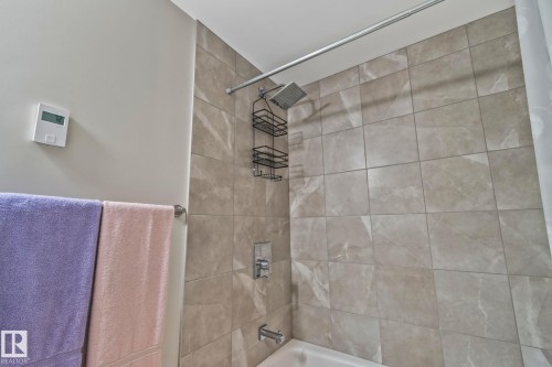 Bathtub with shower, featuring light-toned tile surround, chrome shower fixtures, and a wall-mounted towel bar - #404 2755 109 St Nw, Edmonton, AB 