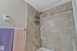 Bathtub with shower, featuring light-toned tile surround, chrome shower fixtures, and a wall-mounted towel bar - 