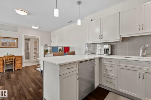 Kitchen featuring white cabinetry, light countertops, stainless steel dishwasher, and a tile backsplash - #404 2755 109 St Nw, Edmonton, AB 