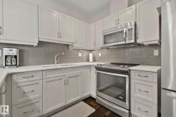 White shaker cabinetry with curved hardware, stainless steel appliances, light-toned countertops, and a gray tile backsplash - 