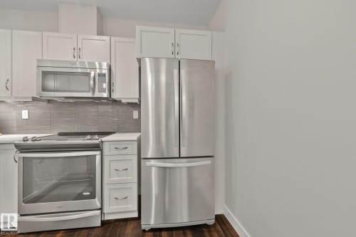 Stainless steel appliance suite, white shaker-style cabinetry, wood-finish flooring, quartz-finish countertops, and a tiled backsplash - #404 2755 109 St Nw, Edmonton, AB 