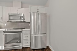 Stainless steel appliance suite, white shaker-style cabinetry, wood-finish flooring, quartz-finish countertops, and a tiled backsplash - 