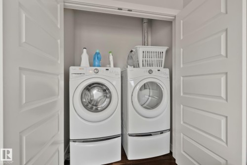 Enclosed laundry area featuring a front-loading washer and dryer set, white paneled bifold doors, and wood-finish flooring - #404 2755 109 St Nw, Edmonton, AB 