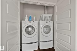 Enclosed laundry area featuring a front-loading washer and dryer set, white paneled bifold doors, and wood-finish flooring - 
