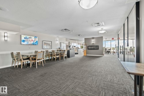 Spacious common area featuring patterned carpet flooring, a wall-mounted fireplace, recessed lighting, and large windows - #404 2755 109 St Nw, Edmonton, AB 