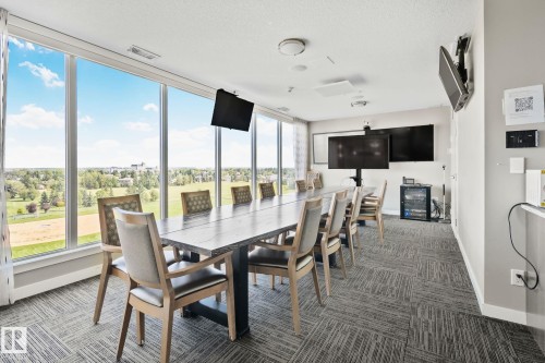 Floor-to-ceiling windows, modern ceiling light fixtures, wall-mounted display screens, built-in media cabinet, and patterned carpet flooring - #404 2755 109 St Nw, Edmonton, AB 