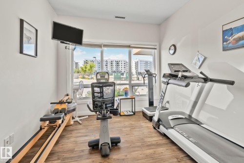 Wood-finish flooring with floor-to-ceiling windows, white walls, and an attached wall-mounted television - #404 2755 109 St Nw, Edmonton, AB 