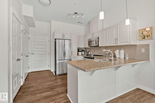 Kitchen featuring wood-finish flooring, light cabinetry, stainless steel appliances, and stone countertops - #404 2755 109 St Nw, Edmonton, AB 