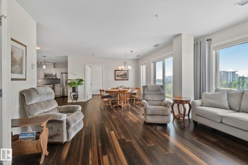 Expansive wood-finish flooring throughout, large windows with curtain rods, and a dining area with chandelier lighting - #404 2755 109 St Nw, Edmonton, AB 