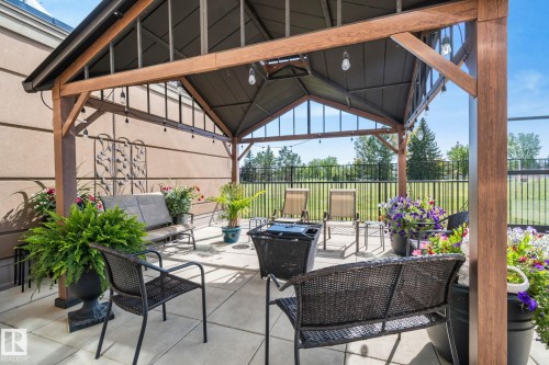 Covered outdoor patio with a concrete slab, featuring a metal gazebo with wood-finish supports, and a black wrought iron fence - #404 2755 109 St Nw, Edmonton, AB 