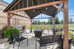 Covered outdoor patio with a concrete slab, featuring a metal gazebo with wood-finish supports, and a black wrought iron fence - 