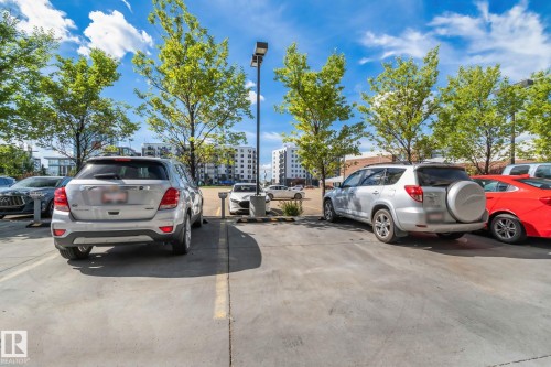 Paved parking area featuring mature trees and street lighting, with multi-story buildings in the background - #404 2755 109 St Nw, Edmonton, AB 