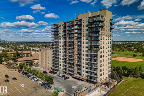 Multi-story building featuring multiple private balconies, a ground-level parking area, and an adjacent green space with a baseball field - #404 2755 109 St Nw, Edmonton, AB 