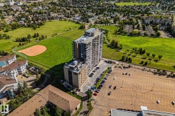 High-rise building with multiple balconies, situated adjacent to expansive green spaces and a baseball diamond - 