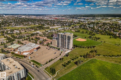 Aerial perspective showcasing a multi-story residential building, adjacent to a large green space with a baseball diamond, and a paved parking area - #404 2755 109 St Nw, Edmonton, AB 