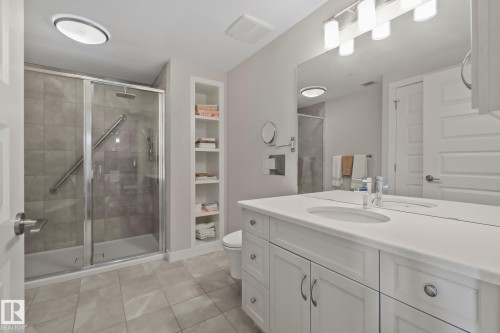 Bathroom featuring a glass-enclosed shower, built-in shelving, a single vanity with an integrated sink, and an expansive mirror - #404 2755 109 St Nw, Edmonton, AB 