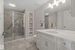 Bathroom featuring a glass-enclosed shower, built-in shelving, a single vanity with an integrated sink, and an expansive mirror - 