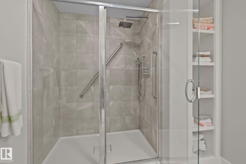 Walk-in shower with tiled walls, integrated grab bars, rainfall showerhead, and built-in shelving unit - #404 2755 109 St Nw, Edmonton, AB 