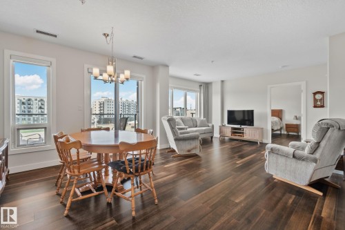 Open-concept living area with dark wood-finish flooring, bright white walls, and a multi-light chandelier - #404 2755 109 St Nw, Edmonton, AB 