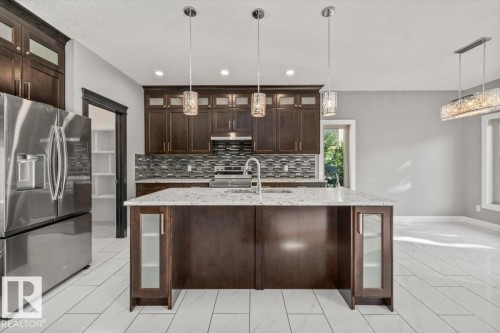 Stainless steel refrigerator, dark wood cabinetry, white countertops, tile backsplash, and light-toned flooring - 1090 Armitage Crescent Sw, Edmonton, AB 