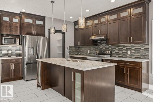Kitchen featuring dark wood cabinetry, a central island with a light-toned countertop, stainless steel appliances, a mosaic tile backsplash, and recessed lighting - 1090 Armitage Crescent Sw, Edmonton, AB 