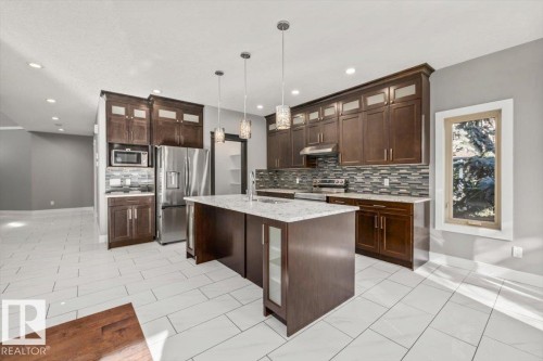 Kitchen featuring dark wood cabinetry, stainless steel appliances, a center island with a light-toned countertop, and white tiled flooring - 1090 Armitage Crescent Sw, Edmonton, AB 