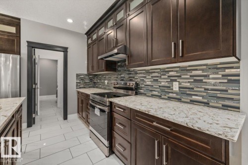 Dark wood-finish cabinetry, stainless steel appliances, patterned tile backsplash, light-toned countertops, and white rectangular floor tiling - 1090 Armitage Crescent Sw, Edmonton, AB 