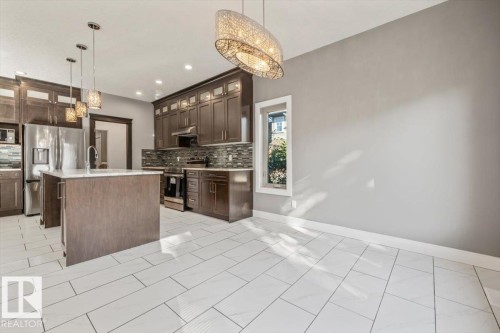 Kitchen featuring dark wood-finish cabinetry, stainless steel appliances, a center island with sink, and tile flooring - 1090 Armitage Crescent Sw, Edmonton, AB 