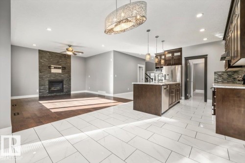 Integrated kitchen and living area featuring a stone-clad fireplace, wood-finish flooring, and a kitchen island with pendant lighting - 1090 Armitage Crescent Sw, Edmonton, AB 