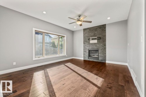 Wood-finish flooring, recessed lighting, ceiling fan, large window, and stone fireplace surround with built-in insert - 1090 Armitage Crescent Sw, Edmonton, AB 
