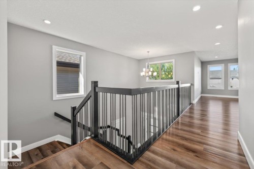Wood-finish flooring throughout, recessed ceiling lighting, black metal balusters, and a contemporary chandelier - 1090 Armitage Crescent Sw, Edmonton, AB 