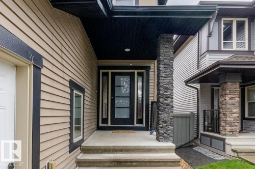 Entryway featuring a stacked stone pillar, concrete steps, and a dark-framed glass paneled door - 1090 Armitage Crescent Sw, Edmonton, AB 