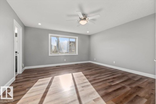 Spacious room featuring wood-finish flooring, a ceiling fan with integrated lighting, recessed lighting, and a large window - 1090 Armitage Crescent Sw, Edmonton, AB 