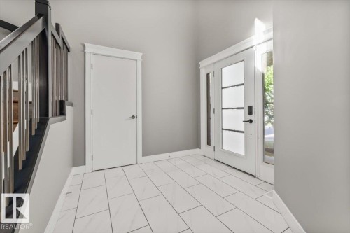 Foyer with rectangular tile flooring, white trim, a solid panel door, and a front entry door with glass panels and sidelights - 1090 Armitage Crescent Sw, Edmonton, AB 