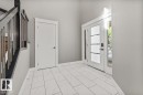 Foyer with rectangular tile flooring, white trim, a solid panel door, and a front entry door with glass panels and sidelights - 1090 Armitage Crescent Sw, Edmonton, AB 