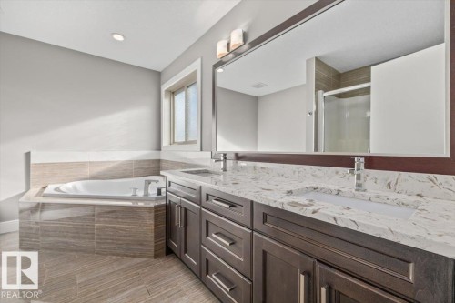 Dual basin vanity with stone countertop, large framed mirror, built-in soaking tub, and tiled flooring - 1090 Armitage Crescent Sw, Edmonton, AB 