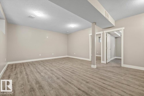 Spacious room featuring wood-finish flooring, light neutral wall paint, and white trim - 1090 Armitage Crescent Sw, Edmonton, AB 