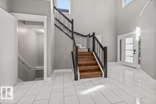 White rectangular tile flooring, wood-finish staircase with black railings, double entry doors with frosted glass, and high ceilings with upper windows - 1090 Armitage Crescent Sw, Edmonton, AB 