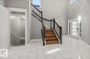 White rectangular tile flooring, wood-finish staircase with black railings, double entry doors with frosted glass, and high ceilings with upper windows - 1090 Armitage Crescent Sw, Edmonton, AB 